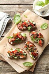 Delicious ricotta bruschettas with tomatoes, arugula and basil on wooden table, flat lay