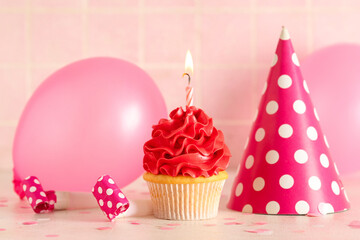 Sweet Birthday cupcake with burning candle, party hat and air balloons on white table