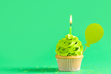 Sweet Birthday cupcake with burning candle on green background