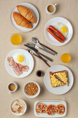 Hearty homemade family breakfast. Eggs, bacon, sausages, beans, croissants, toast and coffee on the table. Top View