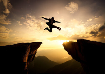 崖を飛び越えるジャンプをするビジネスマンイメージ