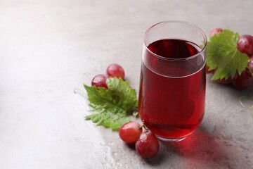 Ripe grapes and glass of tasty juice on grey table