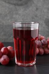 Tasty grape juice in glass and berries on dark textured table, closeup