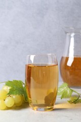 Tasty grape juice in glass, leaves and berries on light table