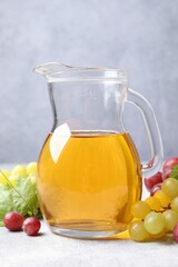 Ripe grapes and jug of tasty juice on grey table