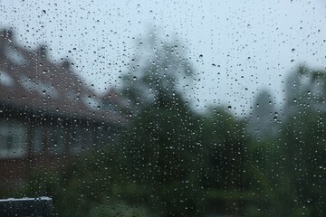 View on buildings through window with water droplets on rainy day, closeup