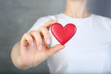 Woman holding red heart on grey background, closeup
