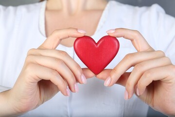 Doctor holding red heart on grey background, closeup