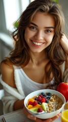 Woman seated at table, holding bowl filled with cereal and fresh fruits. The concept of a healthy breakfast.