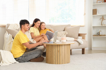 Young man using laptop with two women reading magazine at home. Polyamory concept