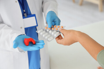 Male endocrinologist with thyroid gland model prescribing pills to mature woman in clinic, closeup