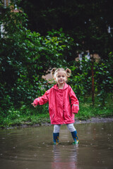 Beautiful girl walking along the puddles under the summer rain in a water-repellent raincoat and...