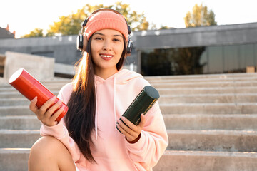 Young Asian woman in headphones with spray paint cans sitting on stairs outdoors
