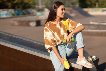 Young Asian woman in headphones with spray paint cans at skate park