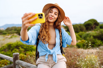 Female travel blogger admires of nature view and shoots video blog on phone. Caucasian woman traveler using mobile phone taking selfie while solo travel in summer sunny day. © maxbelchenko