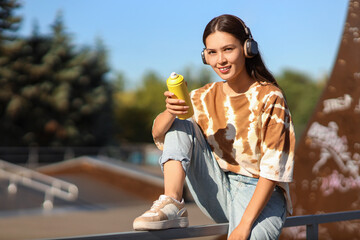 Young Asian woman in headphones with spray paint can at skate park