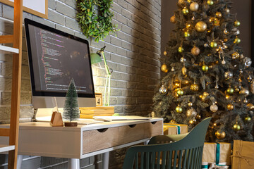 Programmer's workplace with computer and glowing lamp in office decorated for Christmas