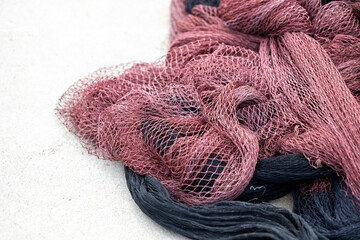 A detailed close-up of tangled fishing nets in maroon and black hues laying on the sandy beach, capturing the texture and intricate patterns of the netting material.