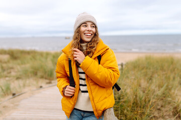 Young woman tourist walking beach on cloudy day. Stylish woman going coastline contemplating life on cold weather.  Active lifestyle.