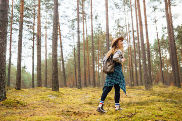 Young woman walks through natural forest. Tourist woman hiking alone in nature at sunset. Active lifestyle. People in forest. Nature, travel, rest concept.