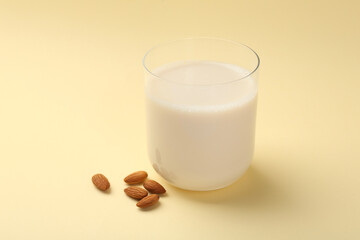 Fresh almond milk in glass and nuts on beige background