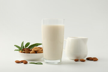 Fresh almond milk in glass, nuts, green leaves and pitcher on white background