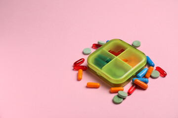 Different pills and organizer on pink background, space for text