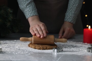 Woman rolling out dough for cookies at light grey marble table, closeup