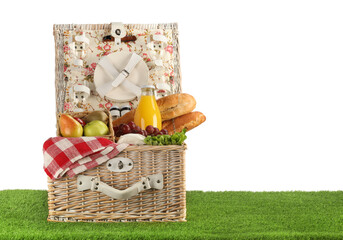 Picnic wicker basket with food, tableware and bottle of juice on grass against white background. Space for text