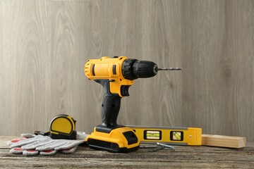 Cordless electric drill, gloves, bits, measuring tape and building level on wooden table