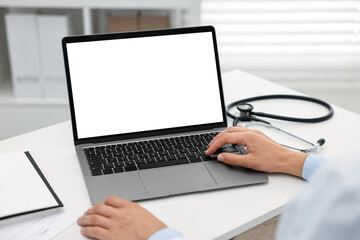 Doctor using laptop at white table in hospital, closeup