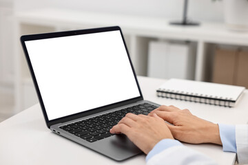Doctor using laptop at white table in hospital, closeup