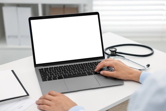Doctor using laptop at white table in hospital, closeup