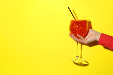 Woman with glass of refreshing cocktail on yellow background, closeup. Space for text