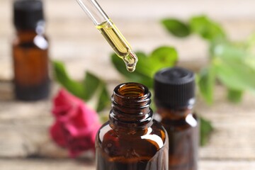 Essential oil dripping from pipette into bottle at table, closeup