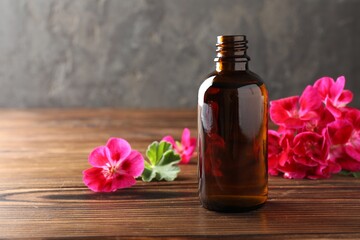 Geranium essential oil in bottle and beautiful flowers on wooden table