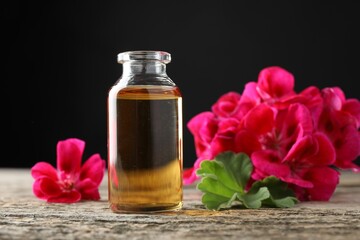 Bottle of geranium essential oil and beautiful flowers on wooden table, closeup
