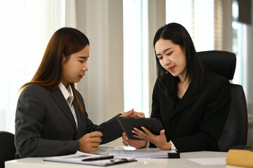 Two young businesspeople having a discussion about new project and using digital tablet at office