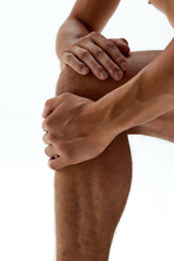 Close-up of fit young man's hands resting on his knee against white studio background. Strength. Concept of body care, male health, natural beauty, youth, masculinity. Ad