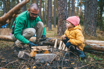 A father and his young daughter work together to build a campfire