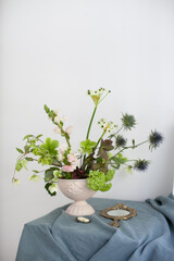 elegant upscale luxury floral arrangement bouquet with green blooms and exotic flowers for home decor, vintage vase and mirror reflection interior decoration with copy space on white wall. 