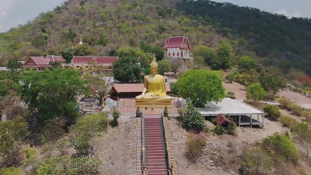 Big Gold Buddha nestled in the mountains with this stunning aerial drone footage. Soar over lush green landscapes of this magnificent statue set against a breathtaking natural. 