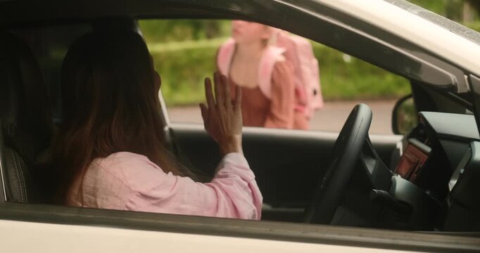 Mom brought her daughter to school by car. Teenage girl with a backpack stands by the window and waves her hand to her mother, blows a kiss. Back to school, the first day after summer holidays.