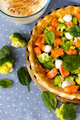 The process of making homemade French quiche pie with broccoli, spinach and salmon on blue plate