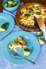 Homemade French quiche pie with broccoli, spinach and salmon on blue plate