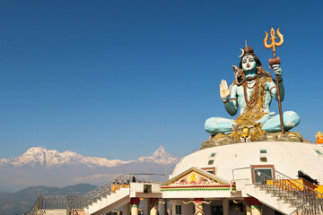 The big statue of Shiva at the Pumdikot Religious Area in front of a mountain range with Mount Machapuchare on the right, close to Phewa Lake, Pokhara, Nepal