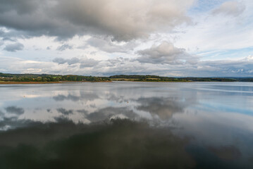 Dam with clouds and sky mirroirng on waterground and countryside on the background - Talsperre Pohl in Saxony