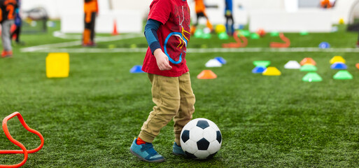 Obraz premium Little children on physical education training at the school field. Children play soccer ball on a training trail with obstacles
