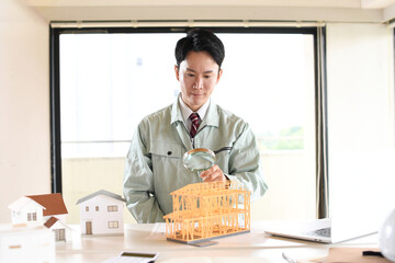 虫眼鏡で建築模型を覗く作業服姿の男性