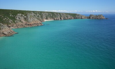 View of Pedn Vounder Beach and Logan Rock surrounded by blue sea. Cornwall, UK.